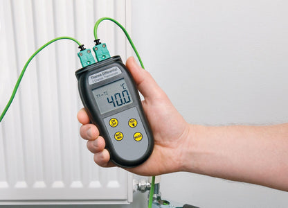 Una persona che tiene in mano un termometro differenziale a due canali di Thermometer.fr davanti a un radiatore.