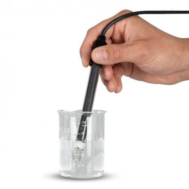 Une main tient un verre d'eau avec un Conductimètre 8500, mesurant les mS/cm et ppm de l'eau.