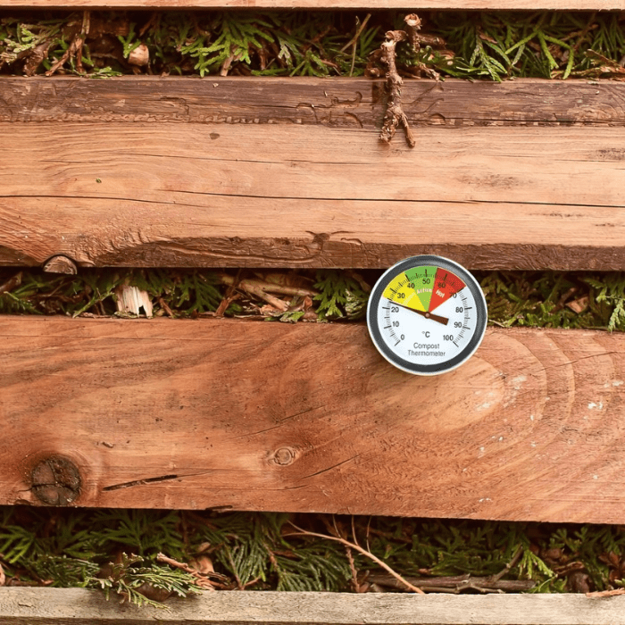 Un Thermomètre.fr thermomètre à compost affichant une lecture de température sur un fond en bois entouré de verdure.