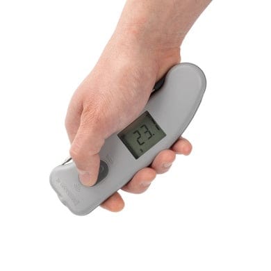 Une main tenant un thermomètre numérique sur fond blanc.