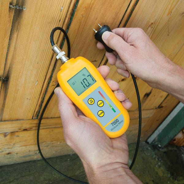 une personne tenant un Thermomètre.fr Testeur d'humidité 7000 avec sonde devant une porte en bois.