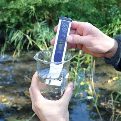 une personne tenant un Testeur de pH PAL Plus de Thermometre.fr devant une rivière.