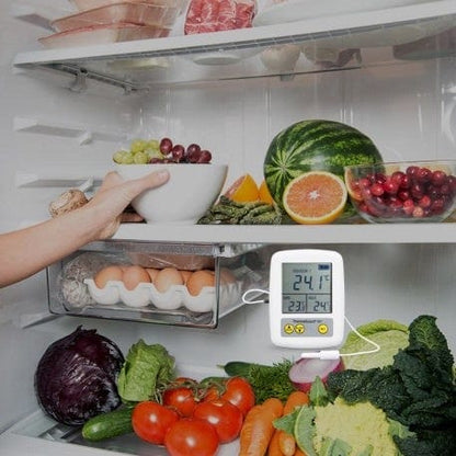 Une personne tenant un thermomètre Enregistreur de surveillance de la température du réfrigérateur ThermaGuard de Thermometre.fr dans un réfrigérateur ouvert.
