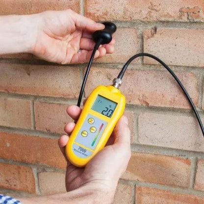 Un professionnel tenant un Humidimètre 7000 avec sonde de Thermomètre.fr devant un mur de briques, tout en utilisant des sondes interchangeables.