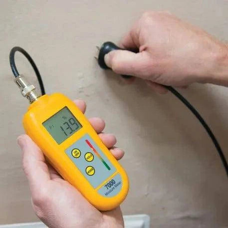 Un professionnel du bâtiment tenant un Humidimètre 7000 avec sonde de Thermomètre.fr sur un mur.